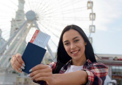 Imagem sobre vistos de turismo mostrando uma jovem segurando seu passaporte em seu país de destino.