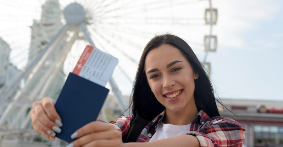 Imagem sobre vistos de turismo mostrando uma jovem segurando seu passaporte em seu país de destino.