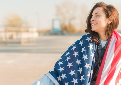 Imagem sobre intercâmbio nos EUA mostrando uma estudante envolta em uma bandeira do país.