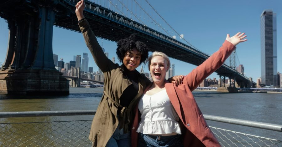 Imagem mostrando duas mulheres felizes e sorridentes, próximas a uma ponte famosa nos EUA, após conseguirem seu green card.