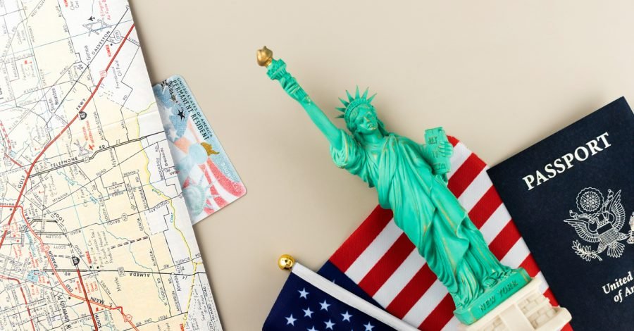 Imagem ilustrando o conteúdo sobre como ter o visto americano aprovado, mostrando um passaporte e uma Estátua da Liberdade sobre uma mesa.