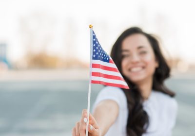 Mulher sorridente, segurando uma bandeira estadunidense, após conseguir seu visto para trabalho nos EUA.