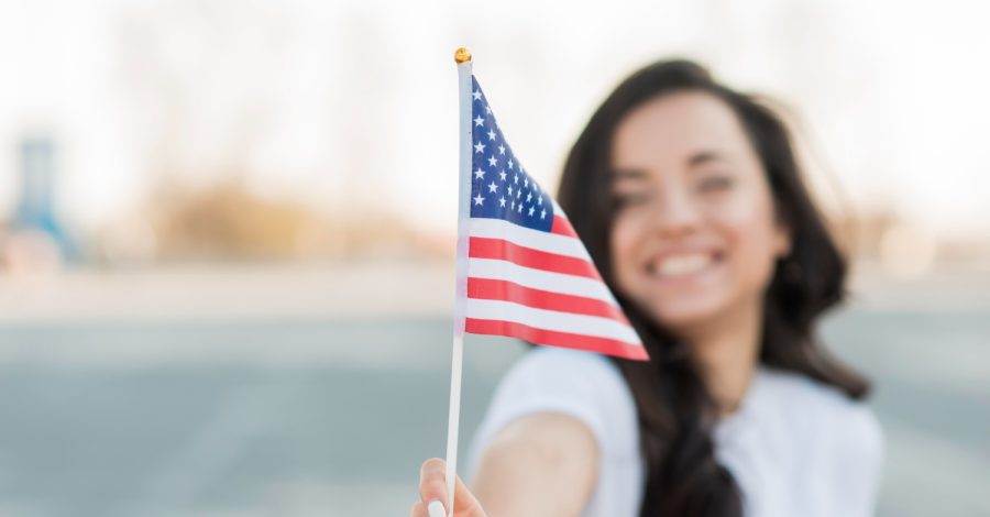 Mulher sorridente, segurando uma bandeira estadunidense, após conseguir seu visto para trabalho nos EUA.